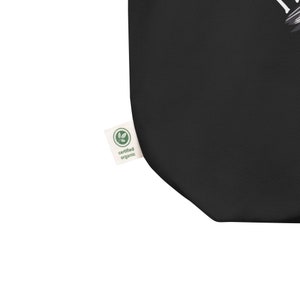 Może przedstawiać: Czarna torba typu tote z białym wzorem graficznym. Torba ma etykietę z napisem "certyfikowany produkt ekologiczny".