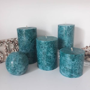 May include: Set of four teal green pillar candles with a marbled effect. The candles are different sizes and are arranged on a white surface.