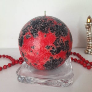 May include: A red and black speckled sphere candle on a clear glass base.
