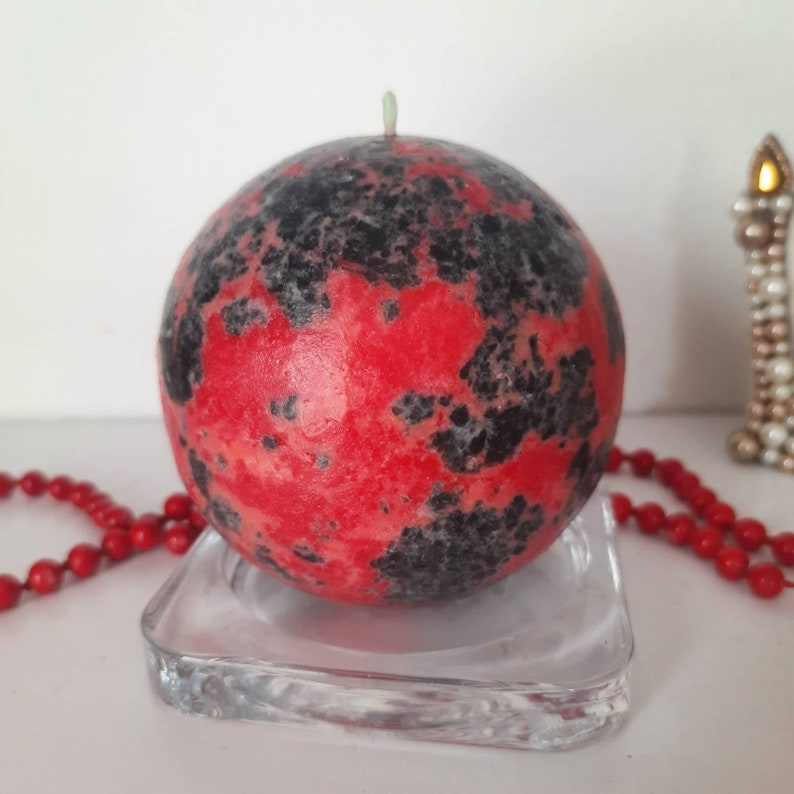 May include: A red and black speckled sphere candle on a clear glass base.