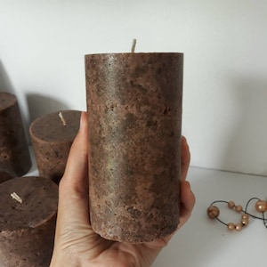 May include: A brown pillar candle with a textured surface. The candle has a white wick.