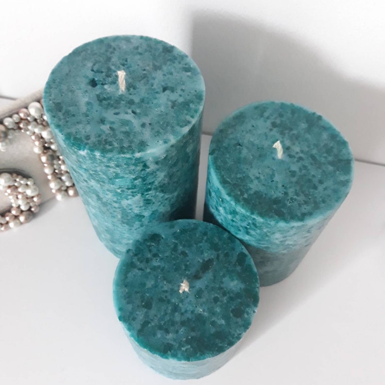 May include: Three teal green pillar candles with a speckled finish and white wicks.