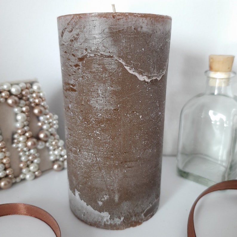 May include: A brown pillar candle with a white distressed finish. The candle is unlit and has a white wick.