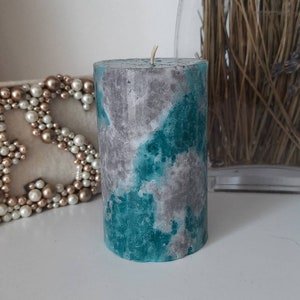 May include: A teal and grey concrete candle with a white wick. The candle has a mottled, marbled appearance.