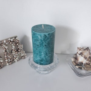 May include: Teal pillar candle with a marbled effect, sitting on a clear glass candle holder.