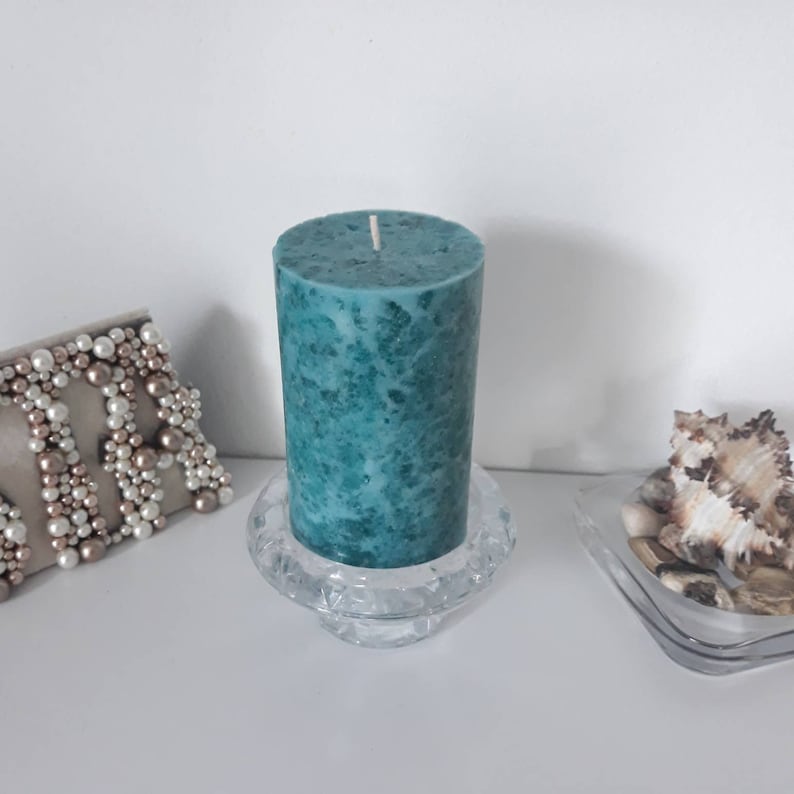 May include: Teal pillar candle with a marbled effect, sitting on a clear glass candle holder.