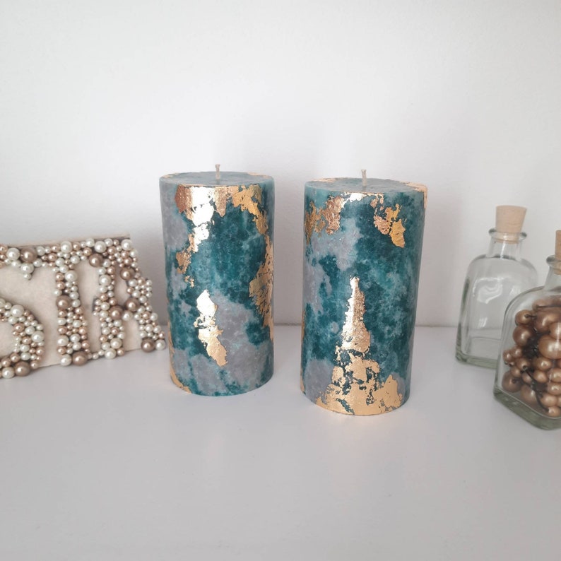 Puede incluir: Dos velas cil&iacute;ndricas con un dise&ntilde;o veteado en verde azulado y gris, acentuadas con pan de oro. Las velas no tienen aroma y tienen una est&eacute;tica sencilla y elegante. Son adecuadas para la decoraci&oacute;n del hogar o como regalo.