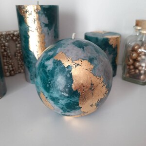 Puede incluir: Colecci&oacute;n de velas decorativas de varias formas. Las velas presentan un dise&ntilde;o veteado en verde azulado y gris con detalles de pan de oro. Una vela es esf&eacute;rica, otras son cil&iacute;ndricas.