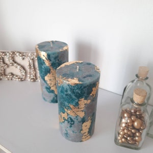 Puede incluir: Dos velas cil&iacute;ndricas de color verde azulado y gris con detalles de pan de oro. Las velas tienen un aspecto veteado y una sola mecha. Botellas de vidrio decorativas con tapones de corcho en el fondo.