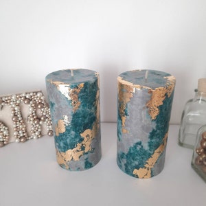 Puede incluir: Dos velas cil&iacute;ndricas con un dise&ntilde;o veteado en color turquesa, gris y pan de oro. Las velas tienen un acabado liso y una sola mecha en la parte superior. Los detalles de pan de oro a&ntilde;aden un toque de lujo a las velas decorativas.