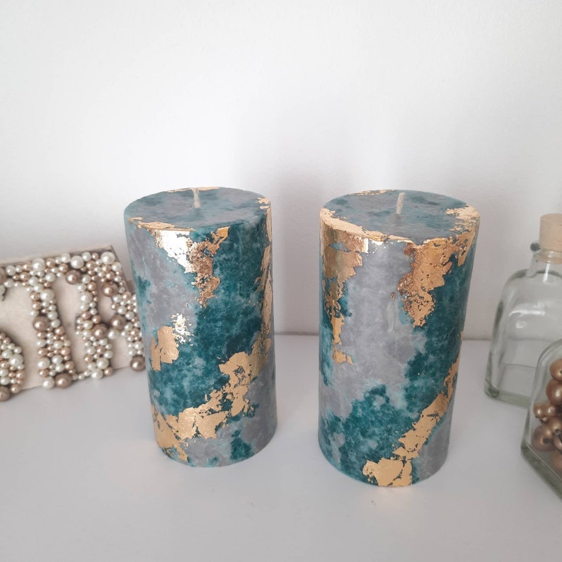 Puede incluir: Dos velas cil&iacute;ndricas con un dise&ntilde;o veteado en color turquesa, gris y pan de oro. Las velas tienen un acabado liso y una sola mecha en la parte superior. Los detalles de pan de oro a&ntilde;aden un toque de lujo a las velas decorativas.