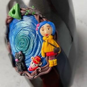 May include: Black ceramic mug with a hand-painted scene featuring a girl with blue hair, a black cat, and a mouse. The scene is set in a forest with a swirling blue background.