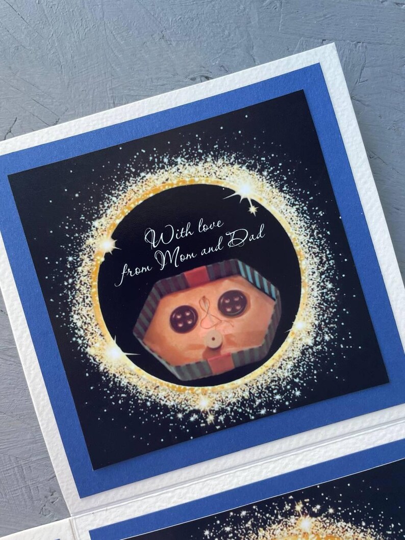 May include: A card with a black background and gold glitter. The card has a picture of a wrapped gift with a face and the text "With love from Mom and Dad".