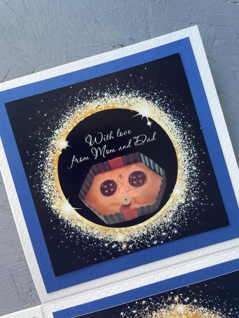 May include: A card with a black background and gold glitter. The card has a picture of a wrapped gift with a face and the text "With love from Mom and Dad".