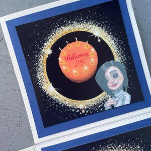 May include: A greeting card with a black background and a sparkly gold ring around a pink cake with the words "welcome 25" on it. A cartoon character with a white turtleneck and a black and white dress is looking at the cake.