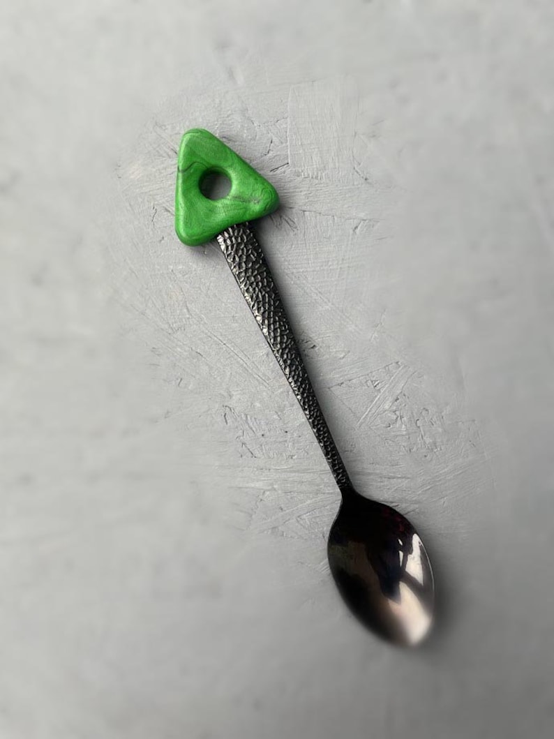 May include: A black metal spoon with a textured handle and a green triangle-shaped handle with a hole in the center.