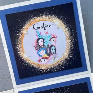 May include: A blue card with a white border and a black background. The card features a circle with a gold glitter effect and the word "Coraline" in a white font. Inside the circle are characters from the movie "Coraline" including Coraline, Other Mother, and the cat.