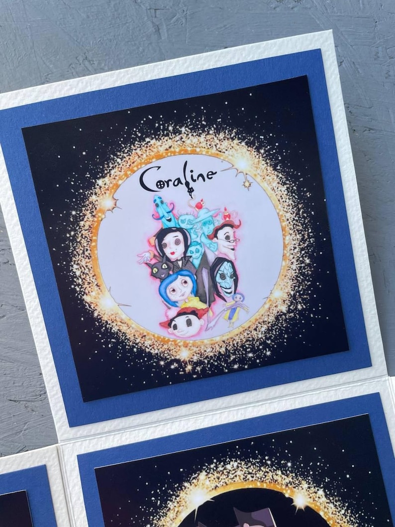 May include: A blue card with a white border and a black background. The card features a circle with a gold glitter effect and the word "Coraline" in a white font. Inside the circle are characters from the movie "Coraline" including Coraline, Other Mother, and the cat.