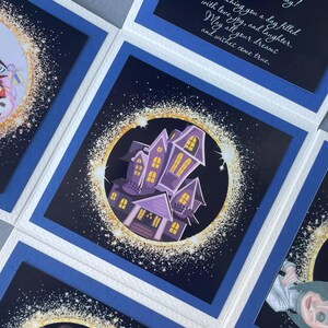 May include: Four different greeting cards with a blue border and a white background. Each card features a different illustration with a dark blue background and a gold glitter effect. The illustrations include a haunted house, a robot, a character from a movie, and a character from a cartoon.