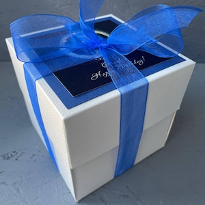 May include: A white gift box with a blue ribbon and a blue and white card that says "Happy Birthday!"