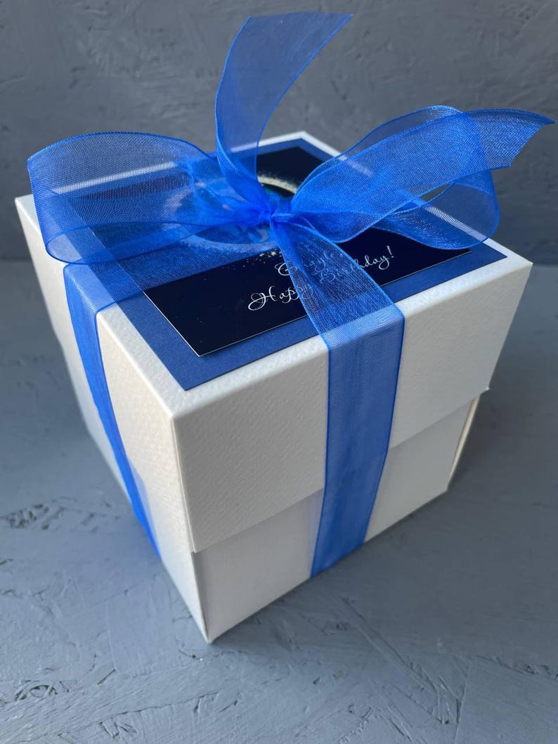 May include: A white gift box with a blue ribbon and a blue and white card that says "Happy Birthday!"