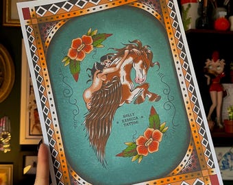 Op de afbeelding: Een print met een vrouw die op een gevleugeld paard rijdt, in een vintage tattoo-stijl. Het kunstwerk heeft een turquoise achtergrond met oranje en zwarte geometrische randen en rode bloemen. De tekst "HOLLY REBECCA TATTOO" is zichtbaar.