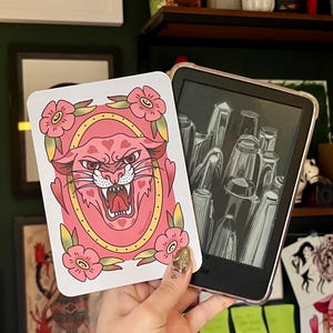 May include: A pink panther with a yellow collar and hearts on its chest is surrounded by pink flowers with yellow centres. The image is on a white card with a gold border.