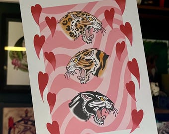 May include: A pink and white print with three black and orange animal heads. The animal heads are of a leopard, a tiger, and a panther. The print is surrounded by red hearts.