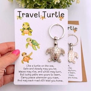 May include: A silver turtle keyring with a card that reads "Travel Turtle." The card features watercolour illustrations of turtles and a poem about journeys. The keyring is attached to a silver ring.