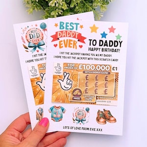 May include: Two birthday cards with the text "Best Dad Ever" and "To Daddy Happy Birthday!" are held in a hand. The cards feature a scratch card design with the text "Top Prizes of £100,000".