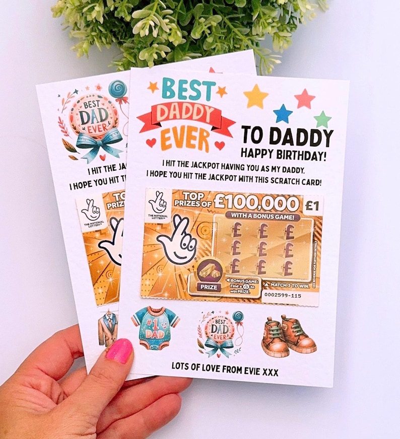 Puede incluir: Dos tarjetas de felicitaci&oacute;n con el texto "Best Dad Ever" y "To Daddy Happy Birthday!" se sostienen en una mano. Las tarjetas presentan un dise&ntilde;o de rasca y gana con el texto "Top Prizes of &pound;100,000".
