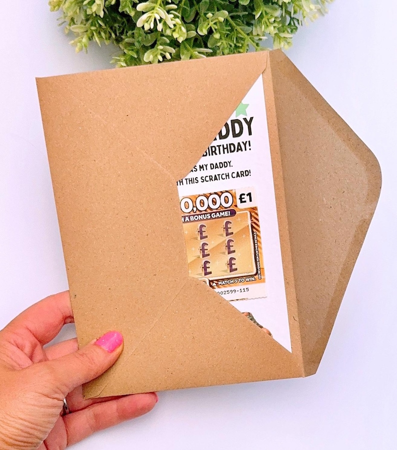 Puede incluir: Un sobre de papel marr&oacute;n con una tarjeta de cumplea&ntilde;os. La tarjeta dice "&iexcl;Feliz Cumplea&ntilde;os Pap&aacute;!" y presenta un juego de rascar con la posibilidad de ganar &pound;1. El sobre est&aacute; sostenido por una mano.