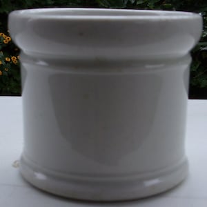May include: White ceramic jar with a rounded top and a slightly flared base. The jar has a smooth, glossy finish.