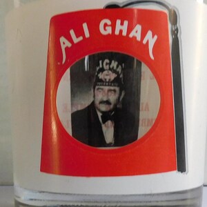 May include: A red and white glass with a black and white image of a man wearing a fez. The glass has the text "ALI GHAN" printed on it.