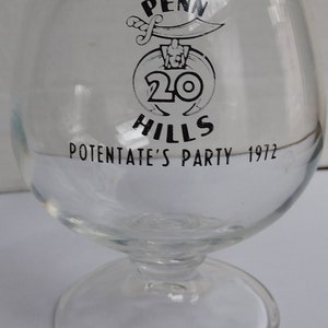 May include: A clear glass goblet with a black and white logo that reads "Penn Hills 20 Potentate's Party 1972".