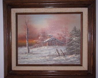 May include: A framed oil painting depicting a snowy winter scene with a small wooden cabin in the distance. The sky is a soft pink and orange, and the trees are covered in snow. The painting is signed "Rodgers" in the lower left corner.