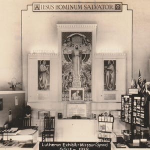 May include: A monochrome photograph of a Lutheran exhibit from 1939. The display includes a central religious mural and panels depicting saints. Tables display brochures and printed matter. The exhibit is labelled "JESUS HOMINUM SALVATOR".