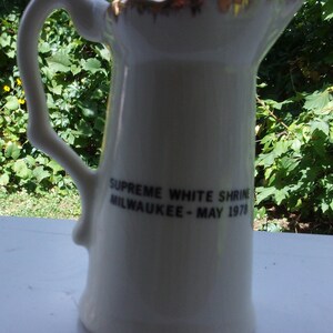 May include: White ceramic pitcher with a gold rim and the text "Supreme White Shrine Milwaukee - May 1978".