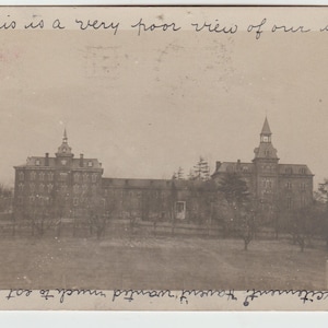 Op de afbeelding: Een zwart-witte vintage ansichtkaart met een uitzicht op een schoolgebouw. De tekst op de ansichtkaart luidt "This is a very poor view of our school."