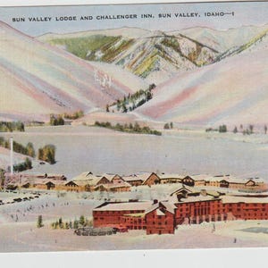 May include: A vintage postcard depicting Sun Valley Lodge and Challenger Inn in Sun Valley, Idaho. The postcard shows a snowy mountain landscape with a cluster of buildings in the foreground.