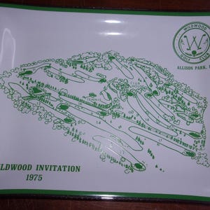 May include: A white rectangular tray with a green border displays a green golf course map. The map includes numbered holes, trees, and the text "Wildwood Invitation 1975." The Wildwood Golf Club logo is in the upper right corner.