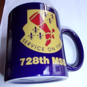 May include: A blue ceramic mug with a yellow and red emblem that says "Service on Time" and "728th MSB".