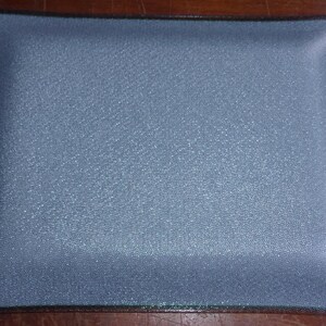 May include: A rectangular, pale blue tray with a textured surface and a dark brown border. The tray's corners are slightly rounded. The tray is likely made of glass or a similar material.