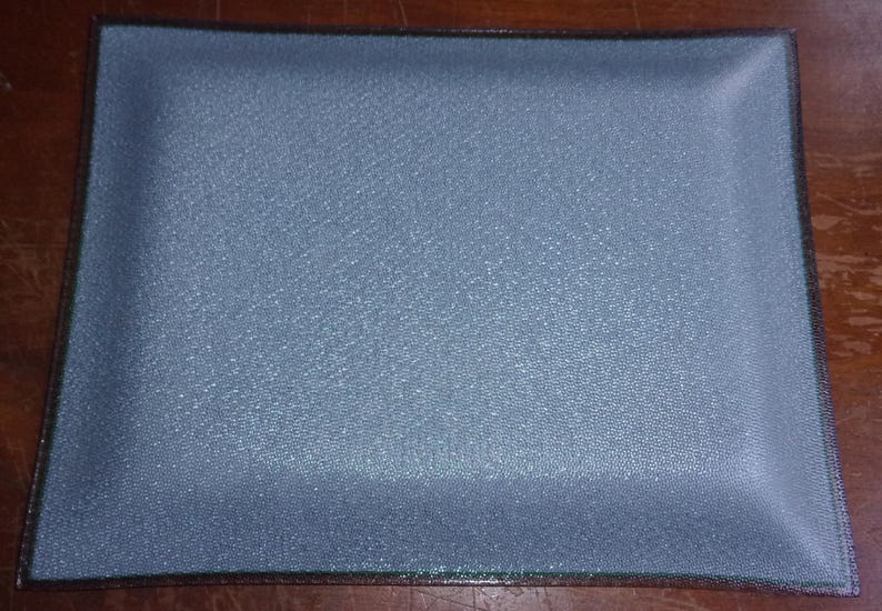 May include: A rectangular, pale blue tray with a textured surface and a dark brown border. The tray's corners are slightly rounded. The tray is likely made of glass or a similar material.