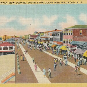 Puede incluir: Postal vintage que representa una vista del paseo mar&iacute;timo en Wildwood, Nueva Jersey. La imagen muestra una calle bulliciosa con tiendas y gente, con una playa y el oc&eacute;ano al fondo. El texto "SAGELS Salt Water Taffy" es visible.