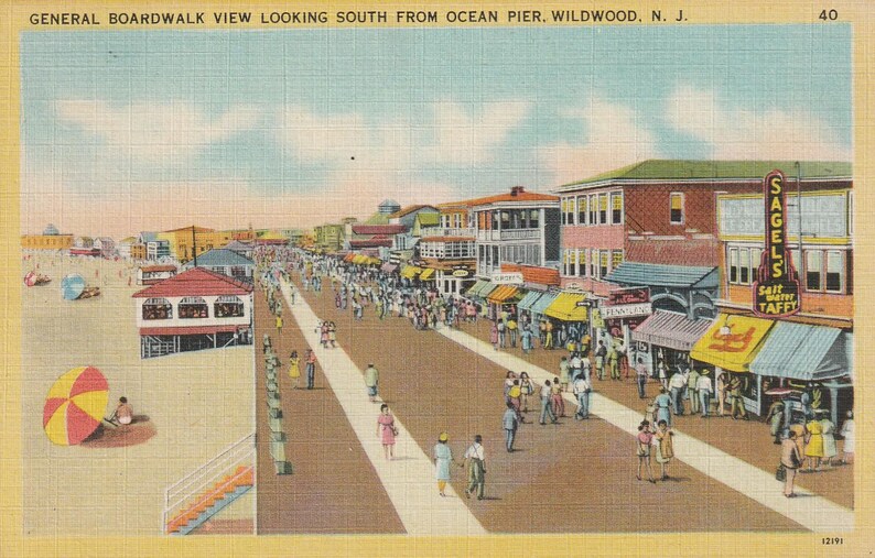 Puede incluir: Postal vintage que representa una vista del paseo mar&iacute;timo en Wildwood, Nueva Jersey. La imagen muestra una calle bulliciosa con tiendas y gente, con una playa y el oc&eacute;ano al fondo. El texto "SAGELS Salt Water Taffy" es visible.
