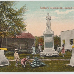 May include: A postcard showing a monument to soldiers in Painted Post, New York. The monument features a statue of a soldier standing on a plinth with an inscription. There are two cannons in the foreground, and a group of children are playing on the grass.