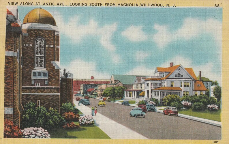 Puede incluir: Postal vintage que representa una escena callejera en Wildwood, Nueva Jersey. La imagen muestra un edificio de ladrillo con una c&uacute;pula dorada, una calle con coches y casas. El texto en la parte superior dice "VIEW ALONG ATLANTIC AVE., LOOKING SOUTH FROM MAGNOLIA, WILDWOOD, N. J."