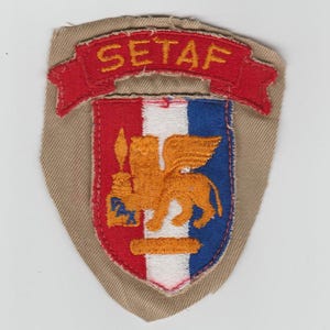 May include: Embroidered SETAF patch featuring a shield design with red, white, and blue sections. A gold lion with wings is centered on the shield. The patch has a red banner with the word "SETAF" in yellow.