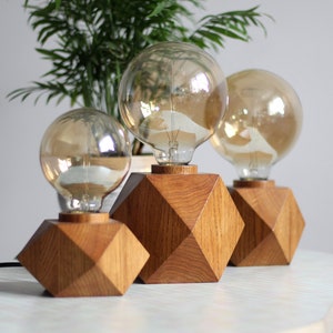 May include: Three wooden geometric lamp bases with clear glass light bulbs. The bases are a dark brown wood with a geometric design. The light bulbs are round and have a warm glow.